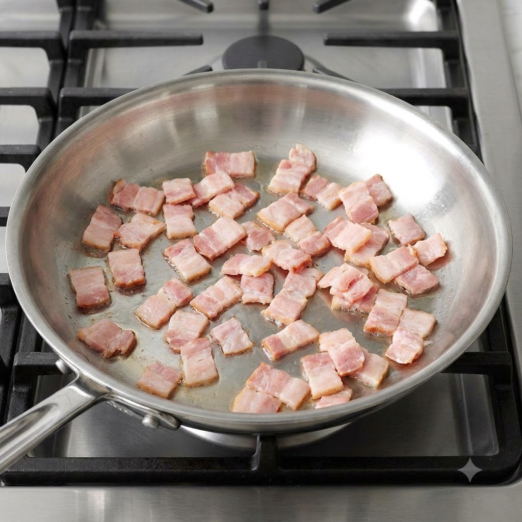 Diced bacon pieces sizzling and browning in a hot stainless steel skillet.