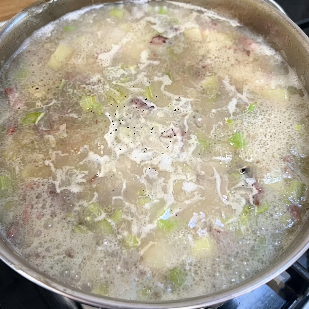 A pot of simmering chowder base with black pepper speckled across the bubbling surface.