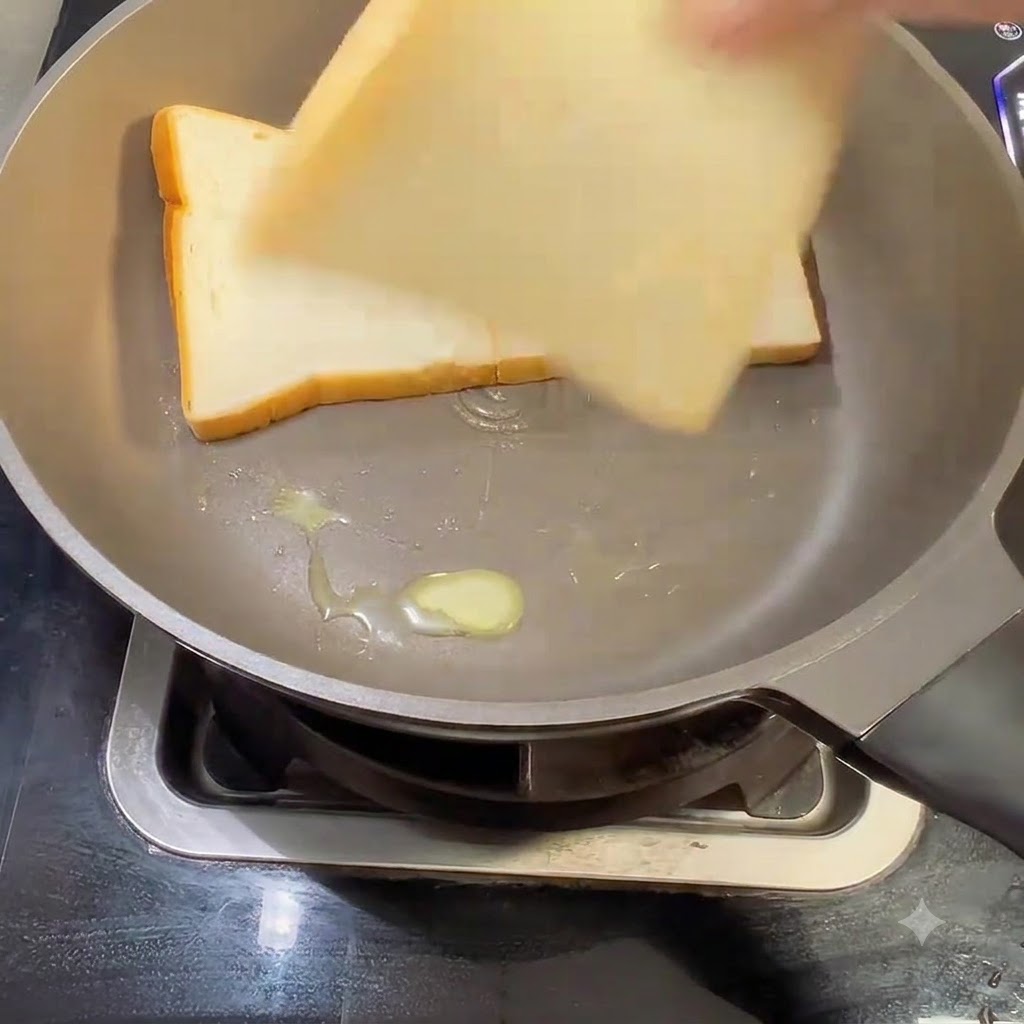 Three slices of white sandwich bread being placed into a buttered frying pan.