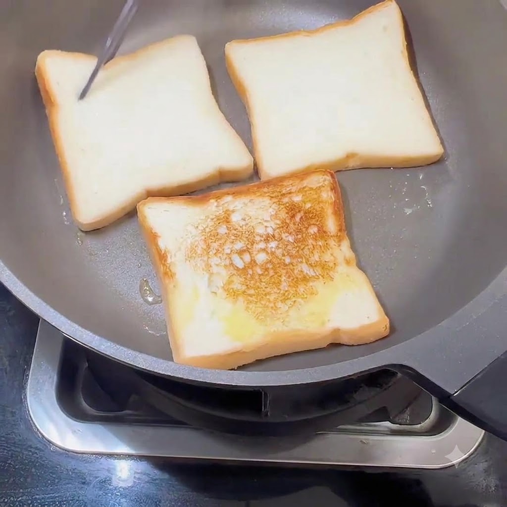 Bread slices being flipped in a skillet, showing a golden-brown toasted crust on one side.