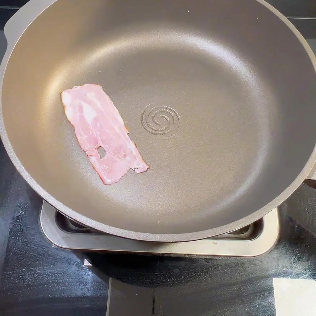 A raw bacon strip placed flat inside a dry frying pan on the stove.