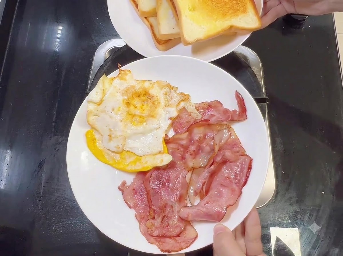 A white plate holding cooked bacon strips and fried eggs, with another plate of toasted bread held above it.
