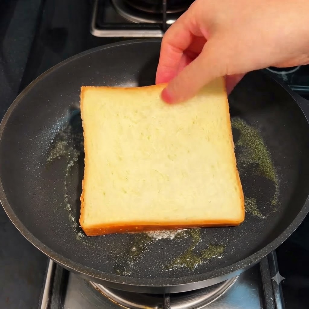 A slice of white bread toasting in a frying pan with butter over a low flame.