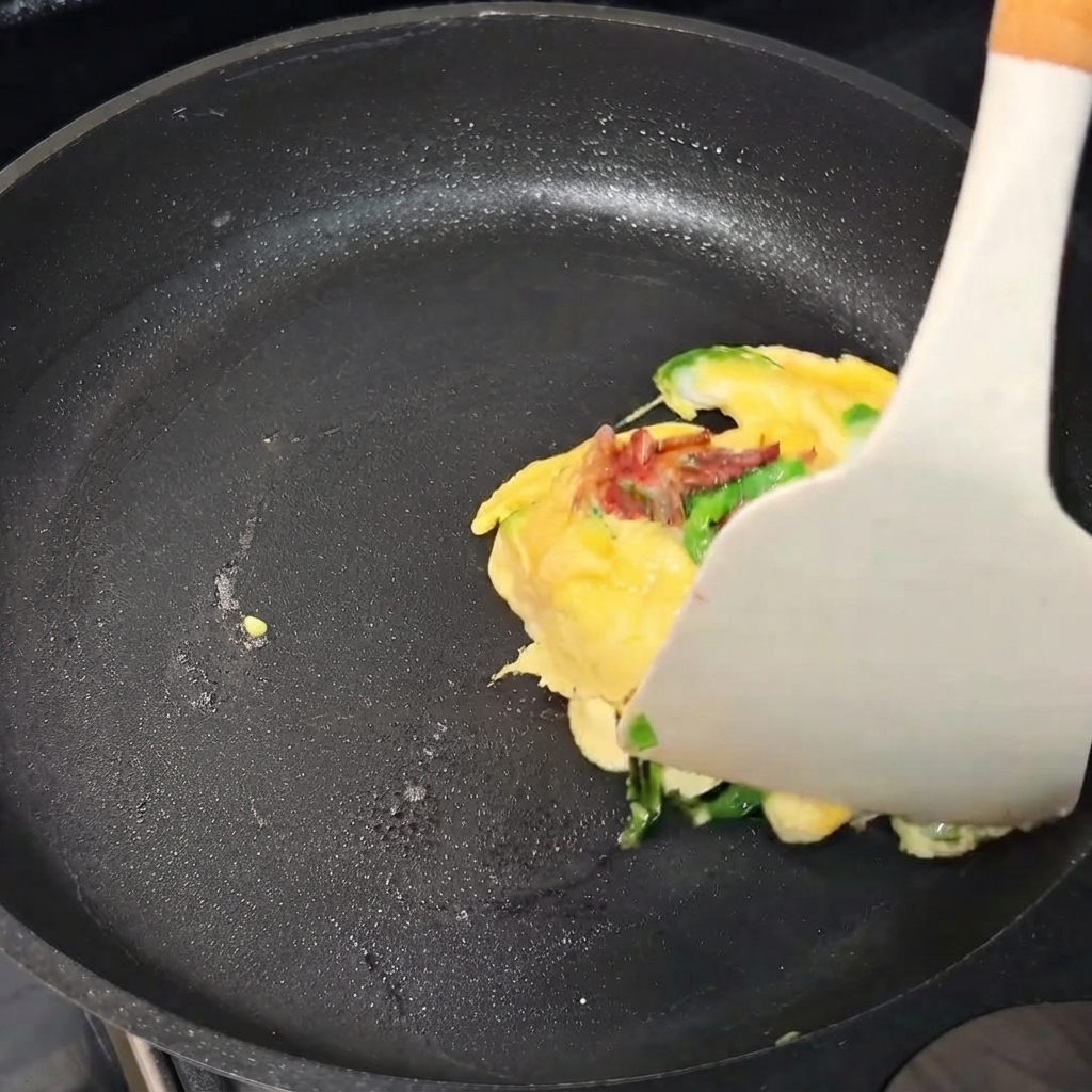 An egg omelet parcel being folded with a spatula inside a frying pan.