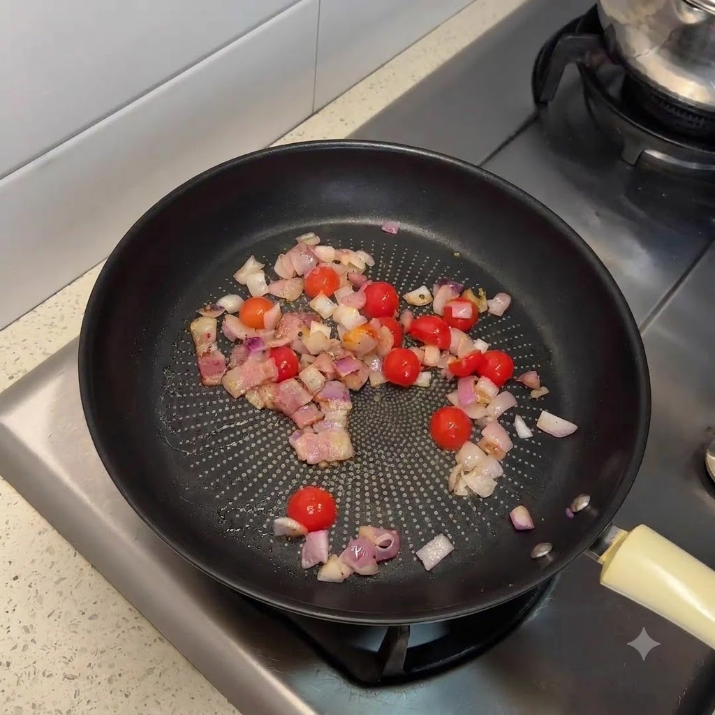 A frying pan filled with sautéed bacon, chopped onions, and halved cherry tomatoes.