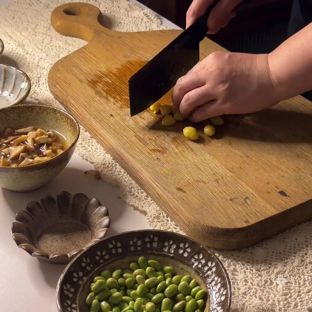 Ginkgo nuts being cut on a wooden cutting board with a cleaver.