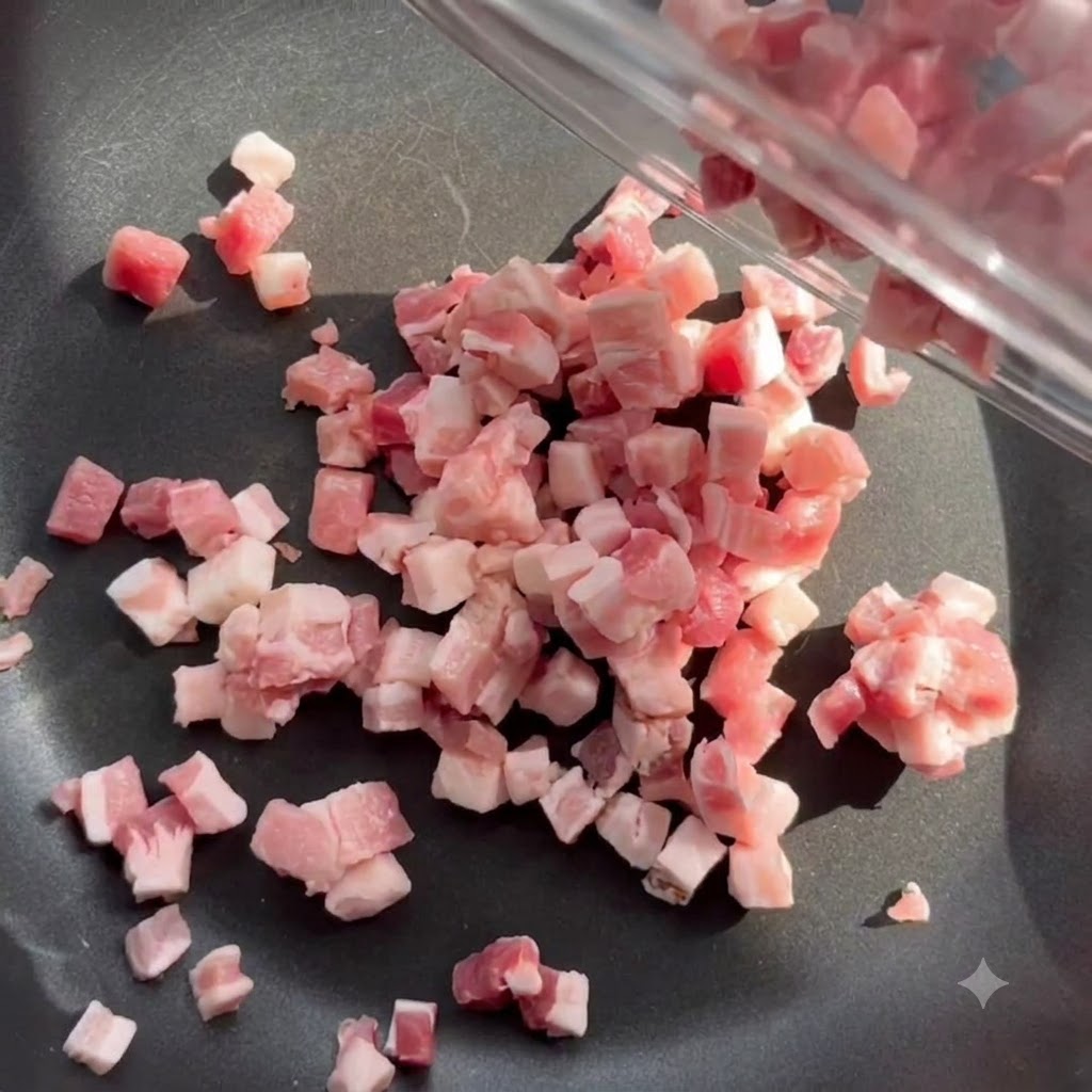 Diced bacon pieces cooking and rendering fat in a black skillet over medium heat.