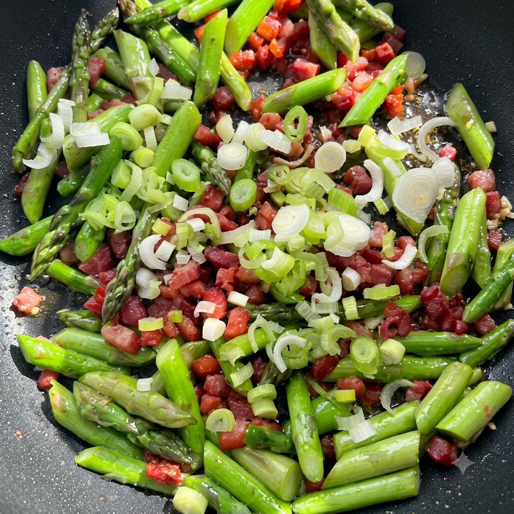 Finely diced garlic and scallion whites scattered over asparagus and bacon in the pan.