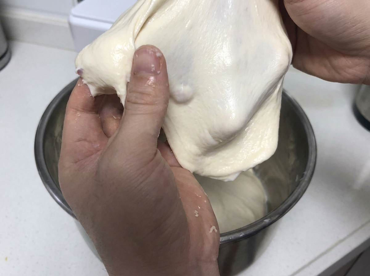 Hands pulling and stretching a soft piece of elastic white dough to demonstrate gluten strength.