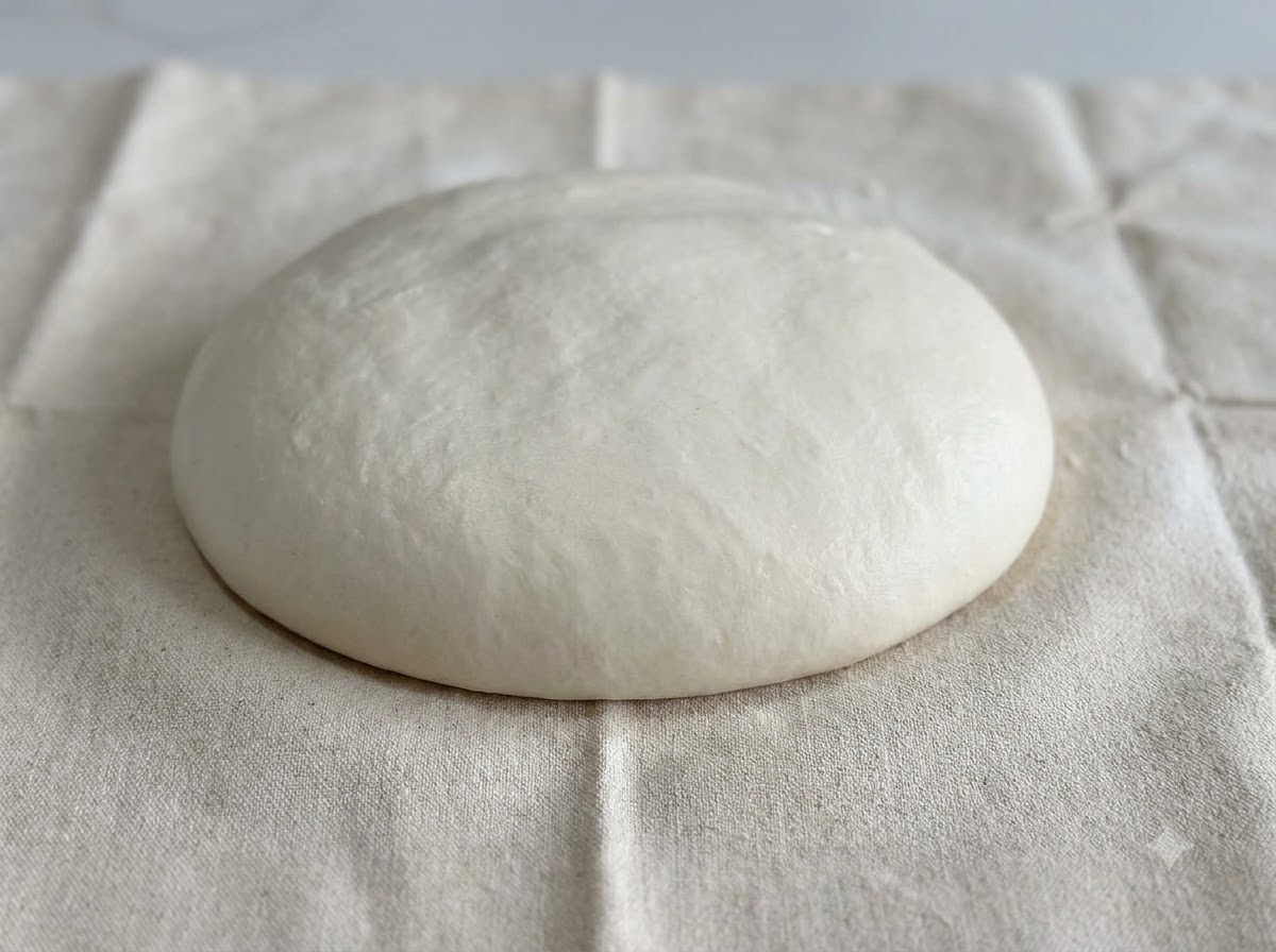 A smooth, rounded dome of white dough resting on a white floured cloth surface.