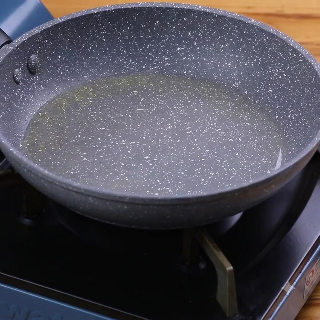 Garlic and green peppers frying in hot oil inside a speckled pan.
