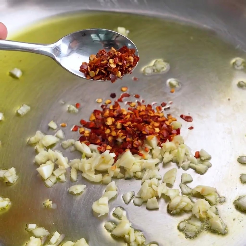 Minced garlic and red pepper flakes sizzling in a stainless steel pan with olive oil.