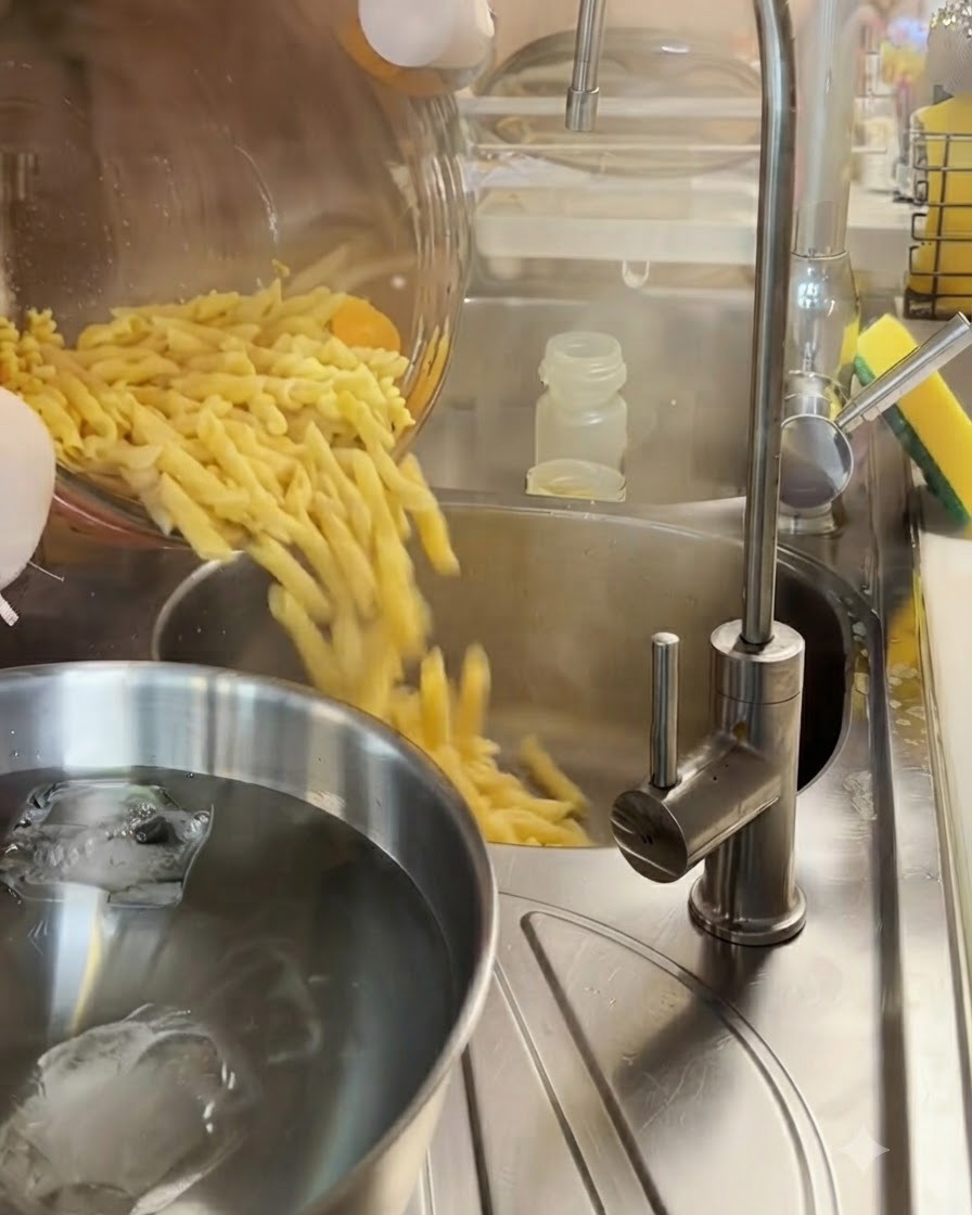 Cooked fusilli pasta being drained in a metal colander over a bowl of ice water.