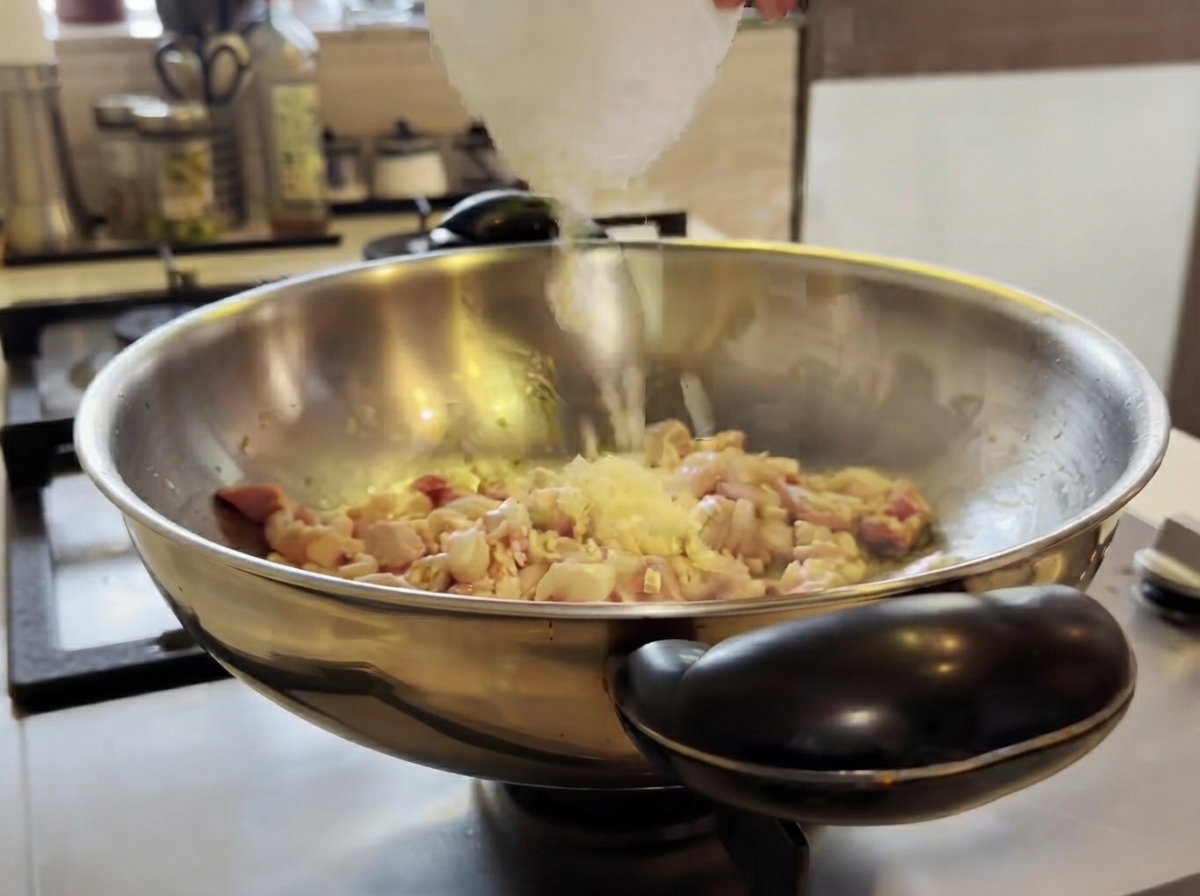 Chopped garlic being added into a wok with cooking chicken and stirred with a spatula.