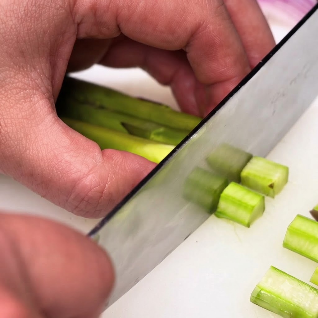 Peeled green asparagus stalks being chopped into small even pieces using a chefs knife.