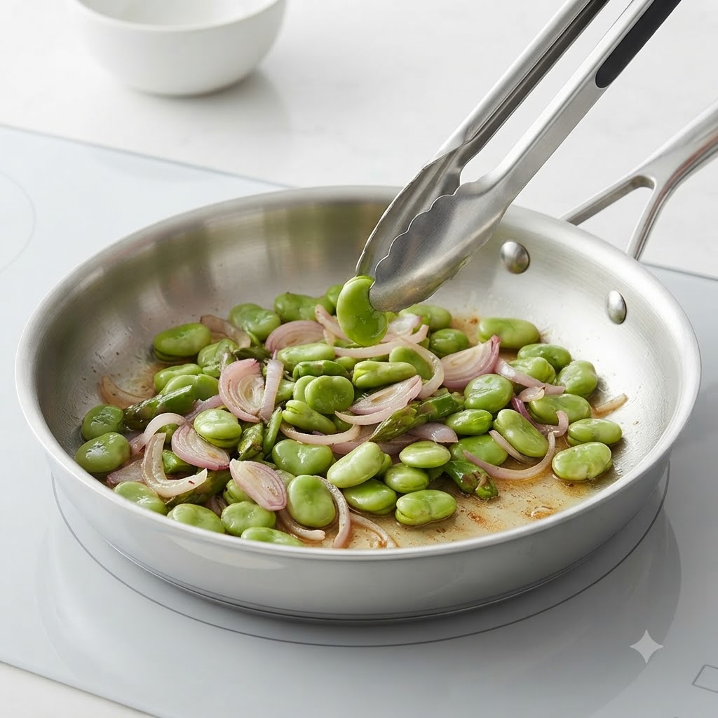 Sliced red onions, asparagus pieces, and broad beans stir-frying in a stainless steel pan.