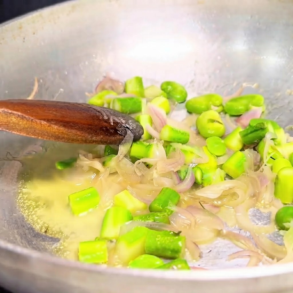 Sautéed onions and green vegetables being scooped out of a metal pan with a wooden spoon.