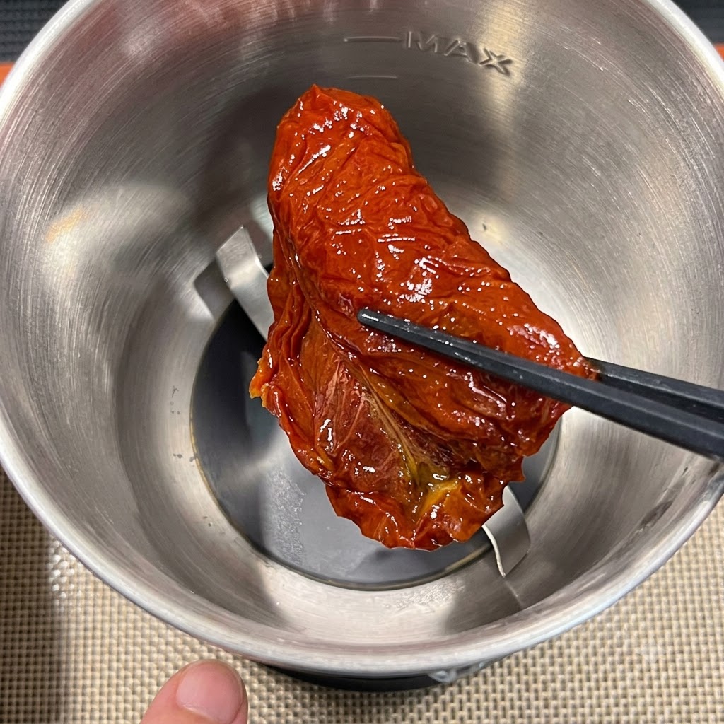 A single piece of sun-dried tomato being placed into a stainless steel food processor attachment using chopsticks.