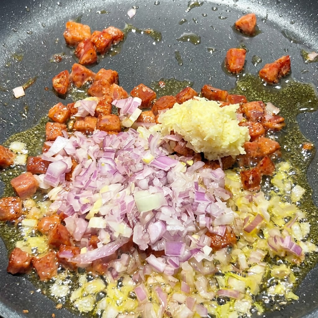Diced red onion and minced garlic being added into the sizzling pan containing browned chorizo pieces.