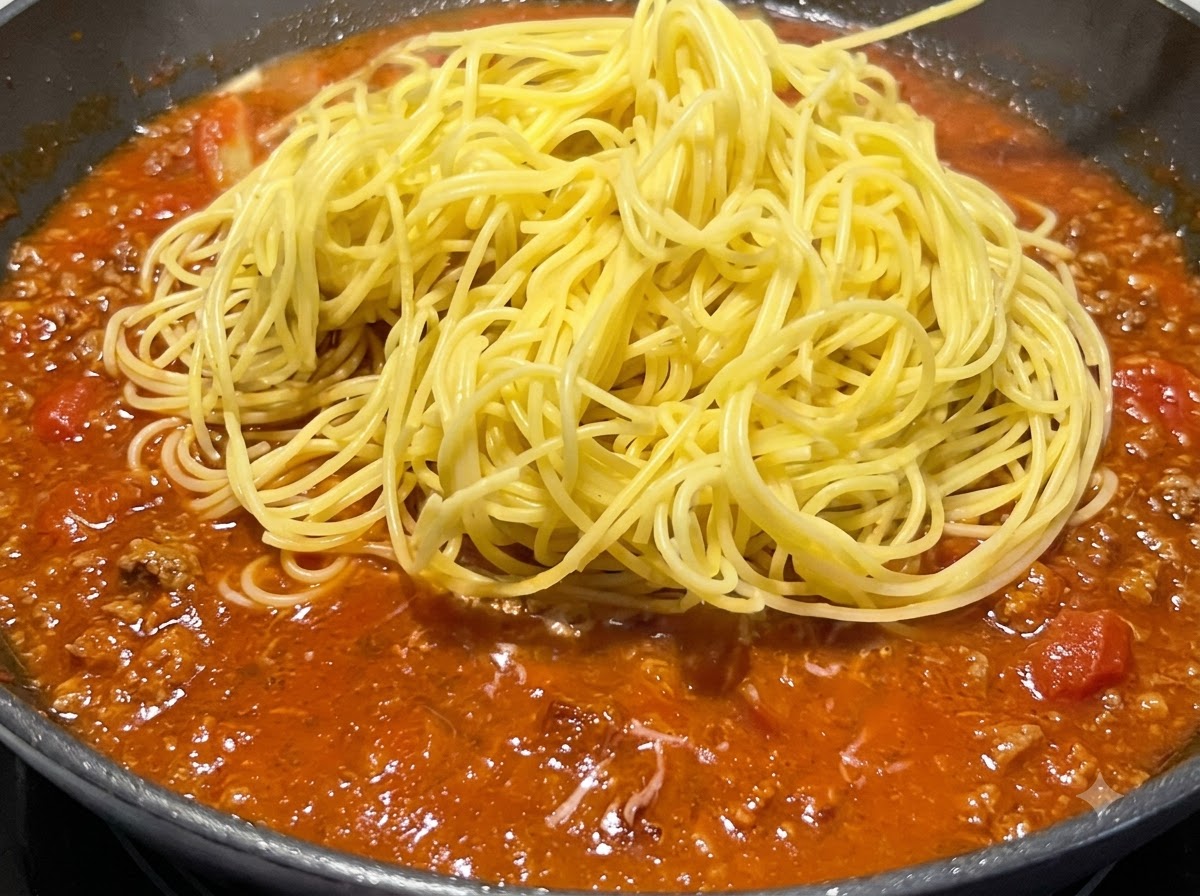 A mound of cooked yellow spaghetti placed on top of the simmering red sauce in a pan.