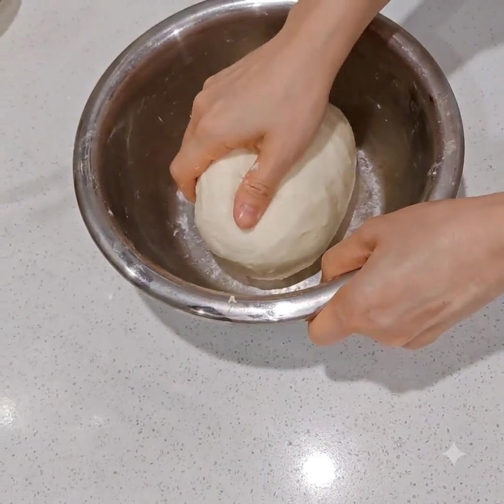 A smooth dough ball being divided into two equal halves using a metal dough scraper.