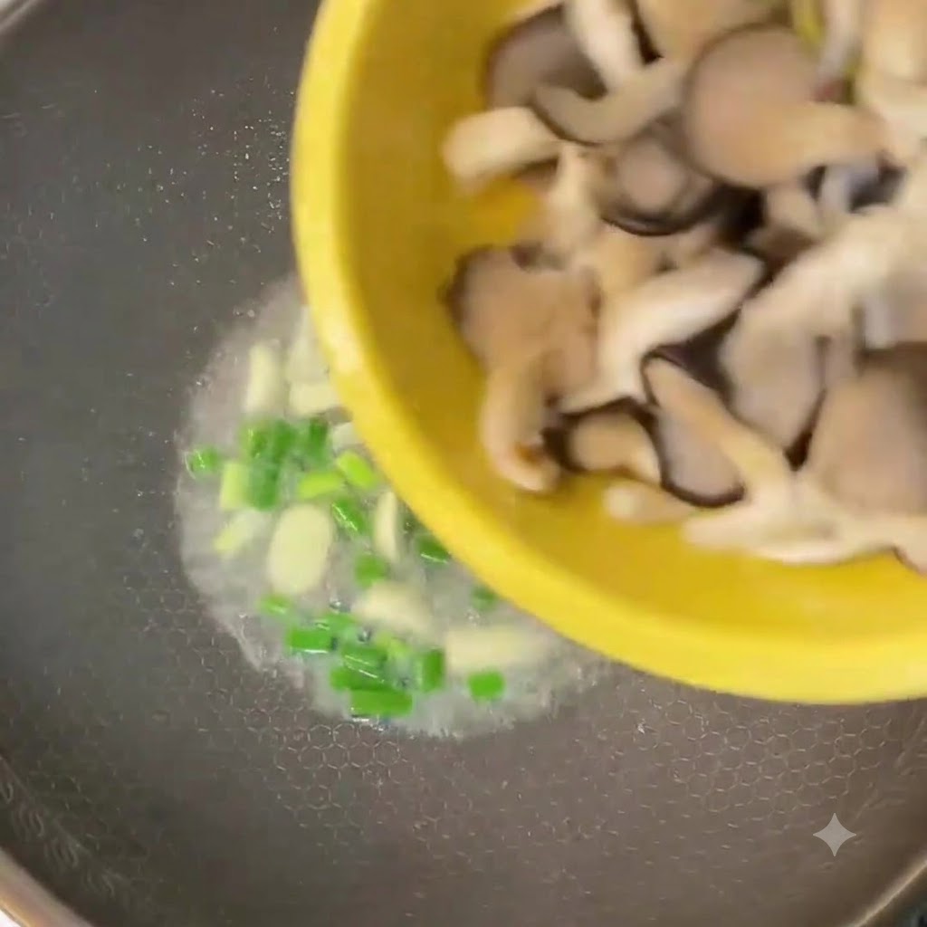 Chopped oyster mushrooms being poured from a yellow bowl into a wok with green onions and garlic.
