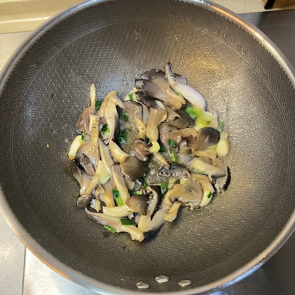 Cooked oyster mushrooms and aromatics being tossed inside the wok.