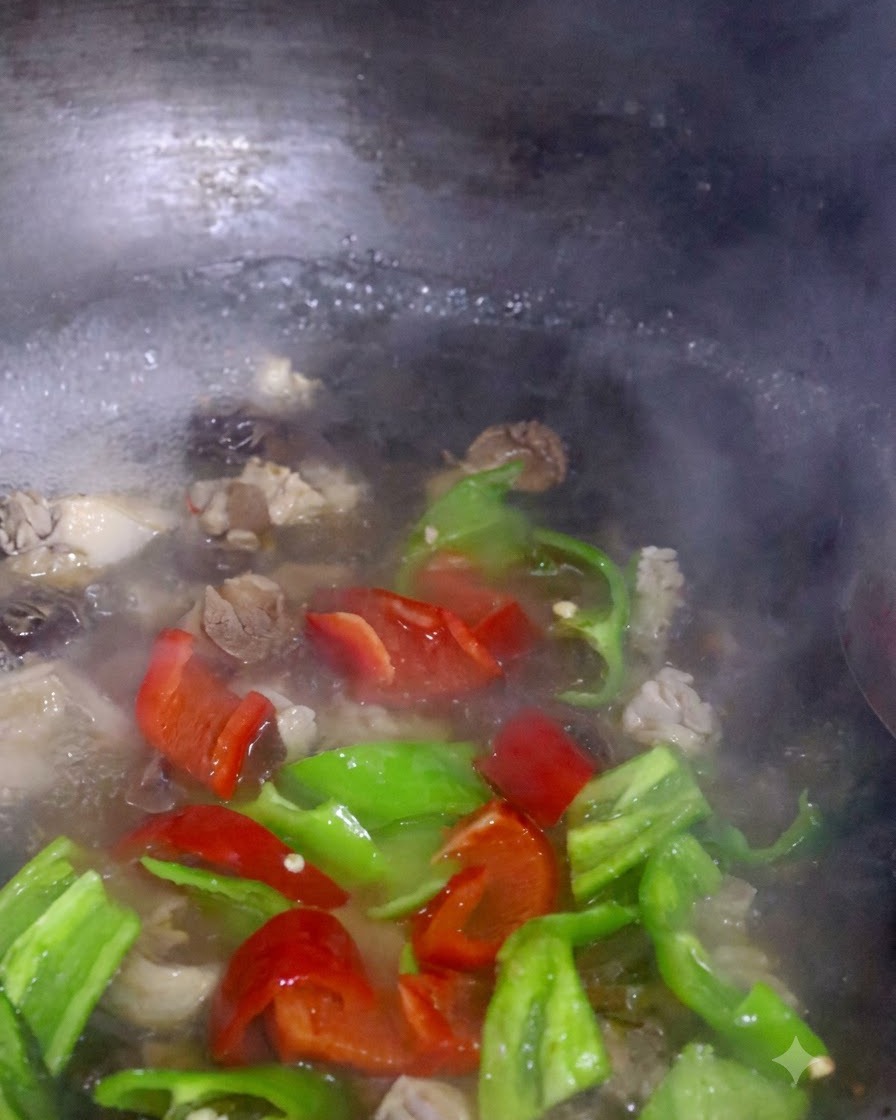 Red and green pepper slices and bok choy boiling together with mushrooms in a pot.