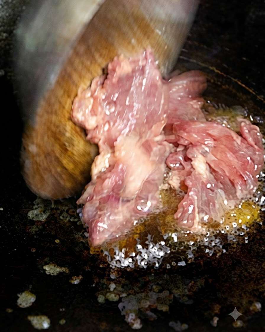 Chopped meat being added to hot oil in a pan using a wooden spatula.