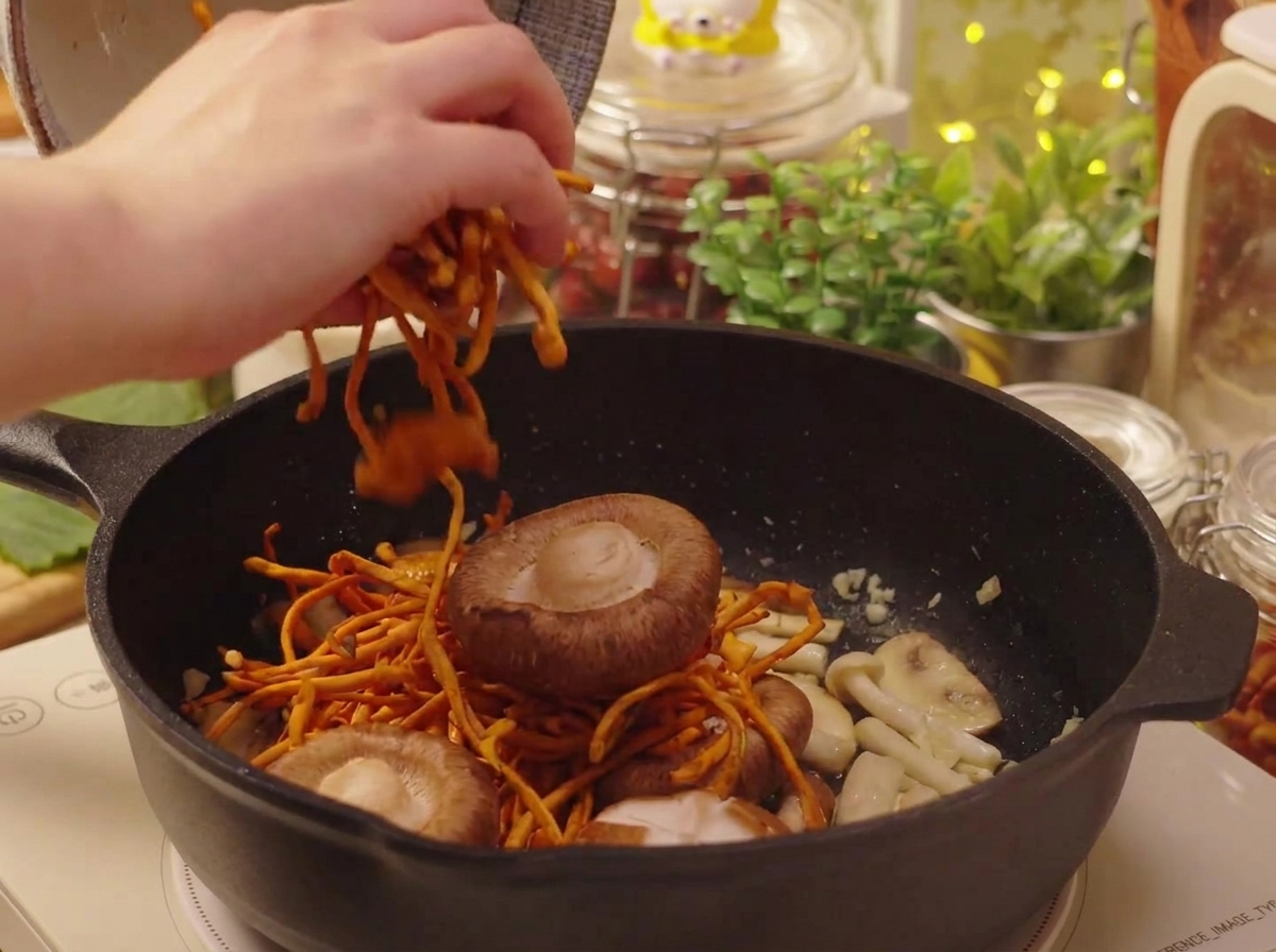 Soaked shiitake mushrooms and cordyceps being added to the pan.