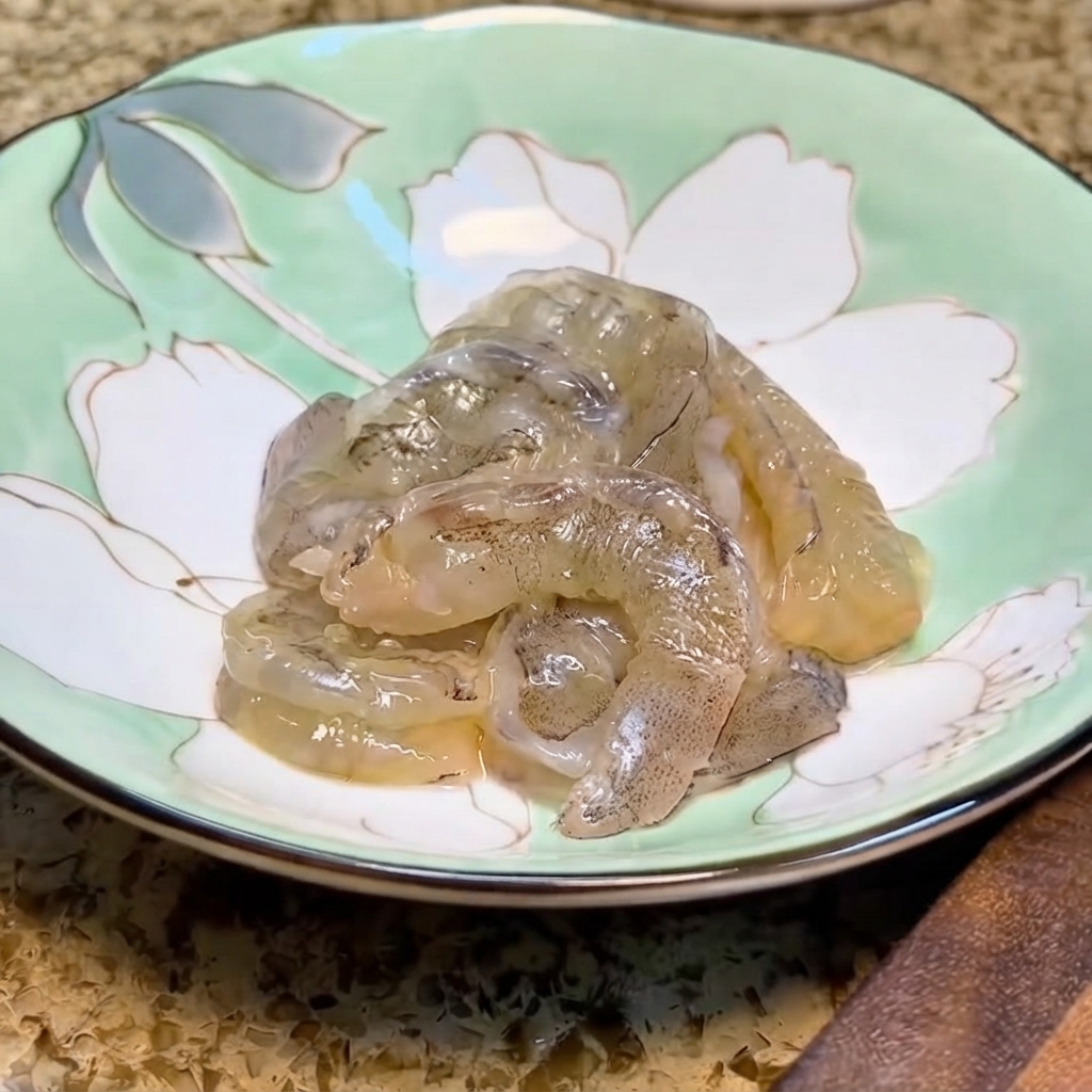 Fresh shrimp sitting inside a light green floral ceramic bowl ready for marinating.
