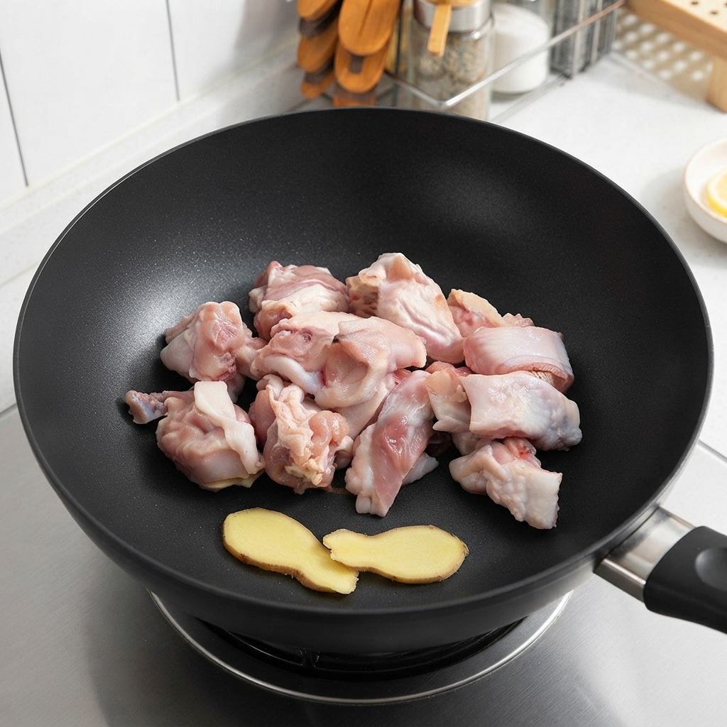 Raw chicken pieces and ginger slices resting in a wok before frying.