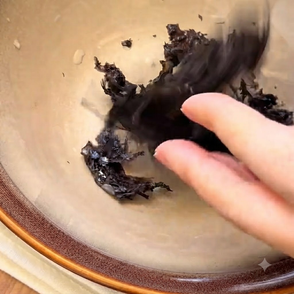 Dried seaweed pieces and white sesame seeds arranged at the bottom of an empty ceramic bowl.