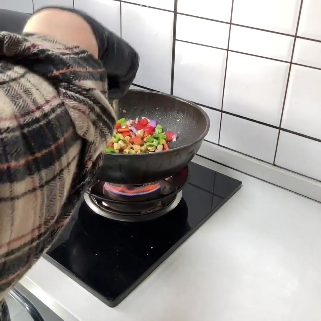 Chopped red and green bell peppers being added directly into the wok containing the stir-fried chicken.