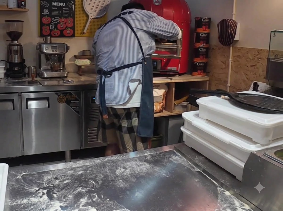 A pizza being loaded into a bright red commercial electric pizza oven using a pizza peel.