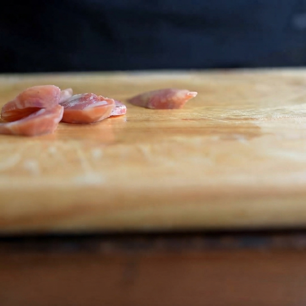 Thinly sliced garlic cloves resting on a wooden cutting board.