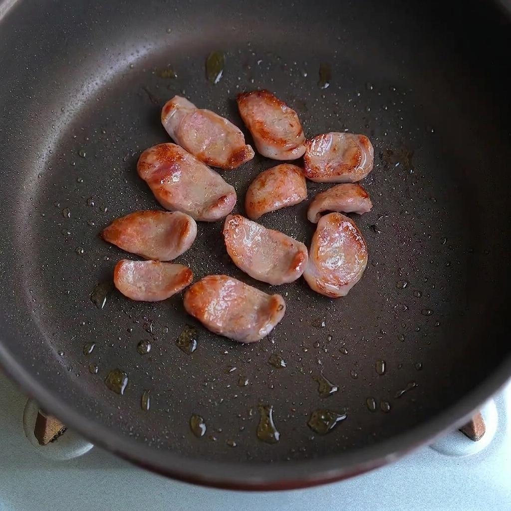 Sausage slices and garlic pieces being tossed together in a frying pan.