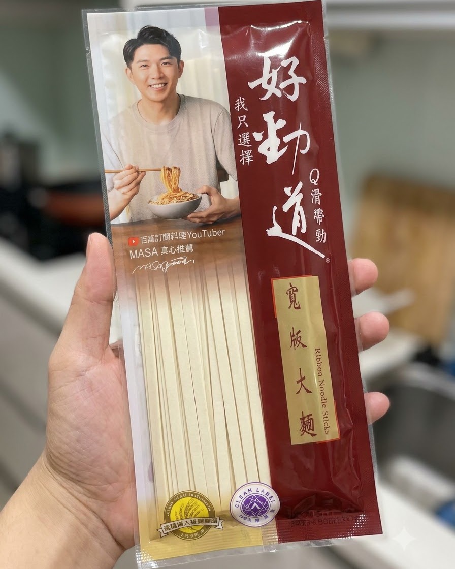 A package of Hao Jin Dao wide ribbon noodle sticks being held in front of a kitchen background.