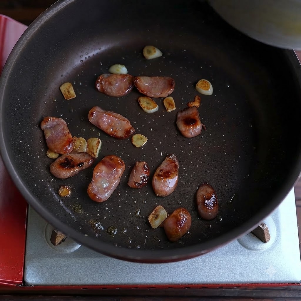 Cooked sausage and fried garlic pieces scattered across the bottom of a frying pan.