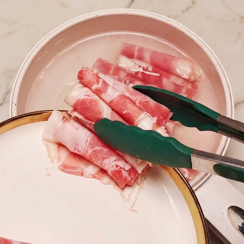 Frozen sliced beef being dropped into a pot of boiling water with green onion sections using tongs.
