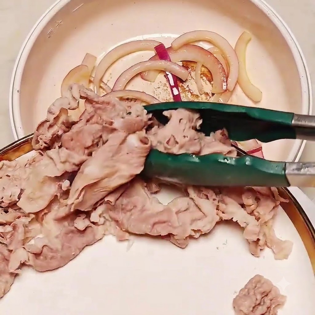 Blanched beef slices being transferred with tongs into a pan containing sautéed onions.