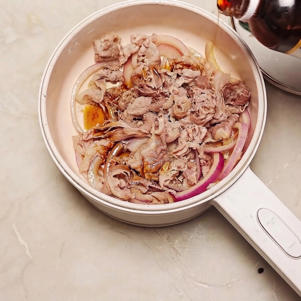 Sukiyaki sauce being poured from a bottle into a pan filled with beef and red onion slices.