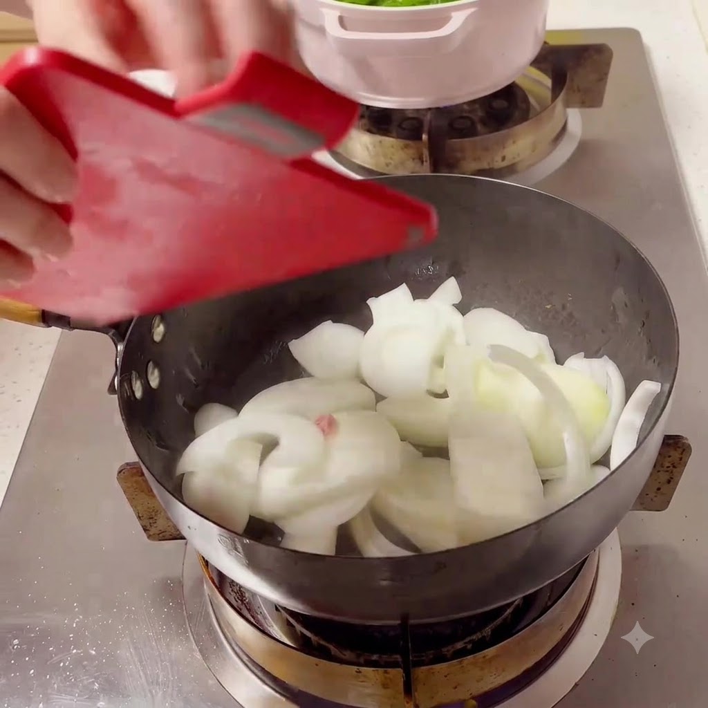 White onion slices being poured from a red cutting board into a hot black wok on a stove.