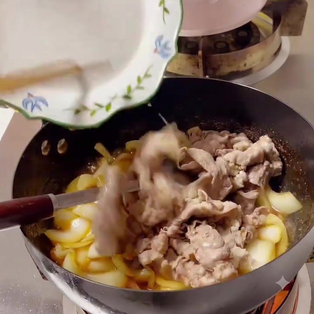 Cooked beef slices being slid off a white plate into a wok filled with onions and sauce.