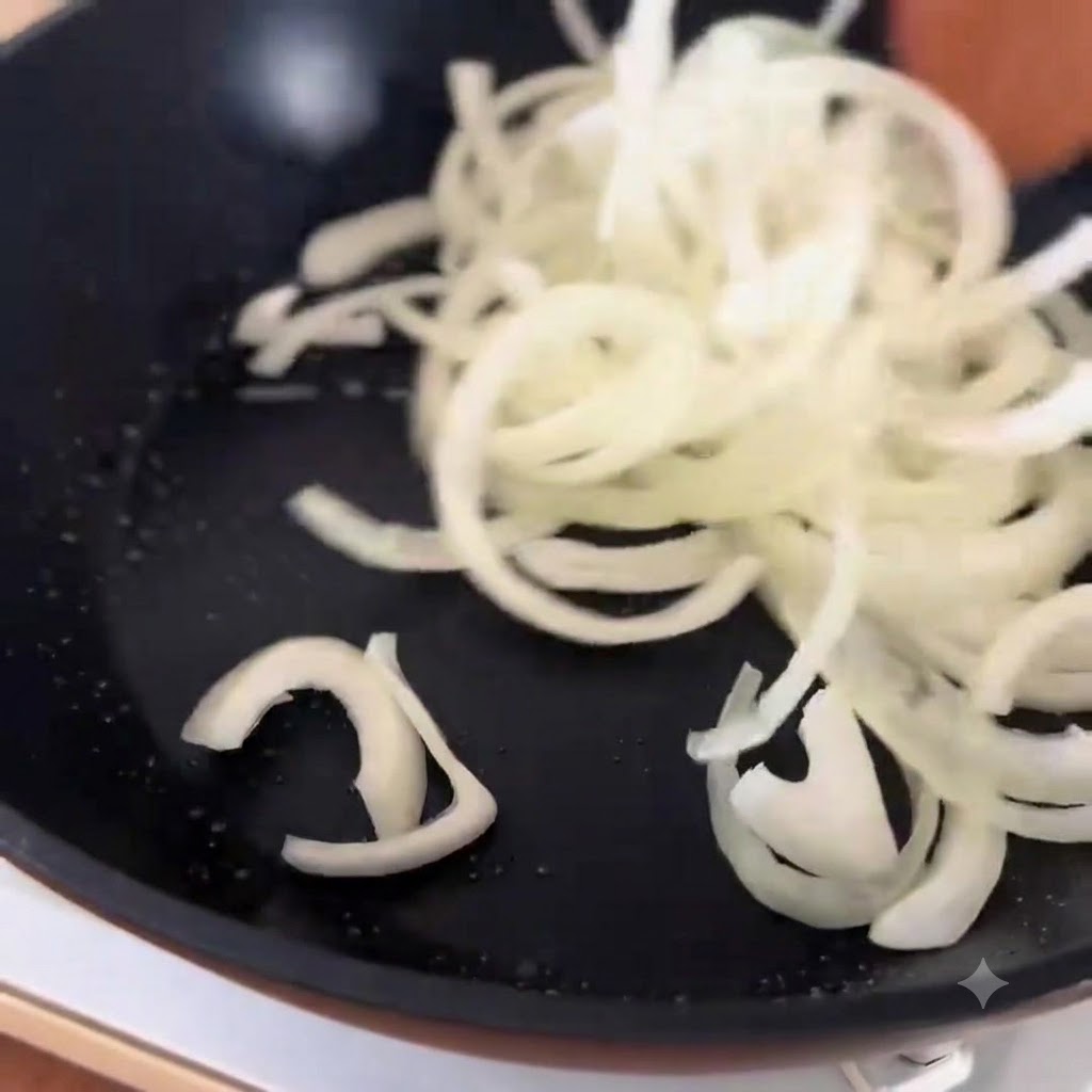 Blanched beef slices being tossed over cooked onions in a skillet.