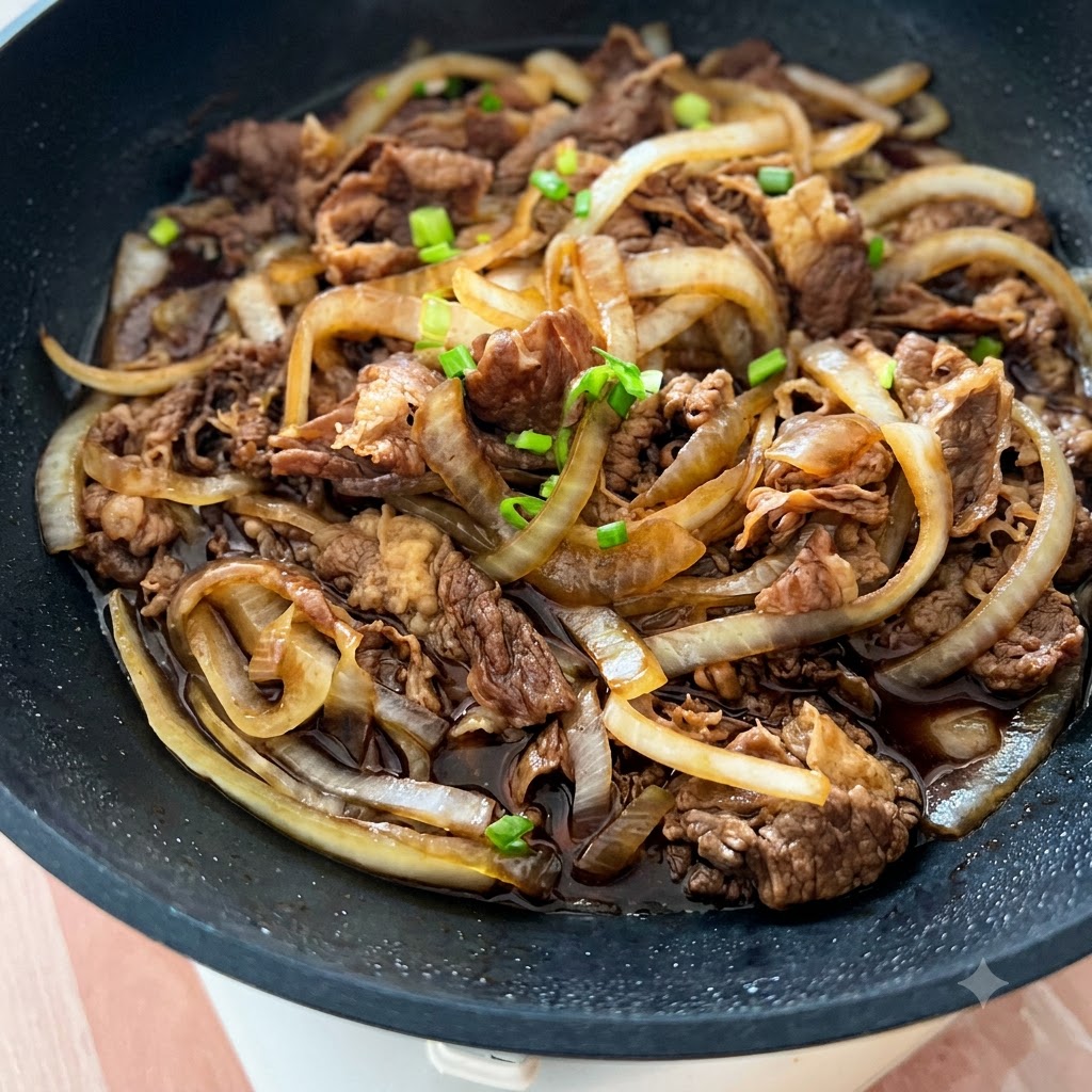 A pan filled with cooked beef and onions, garnished with scattered green onion pieces and white sesame seeds.