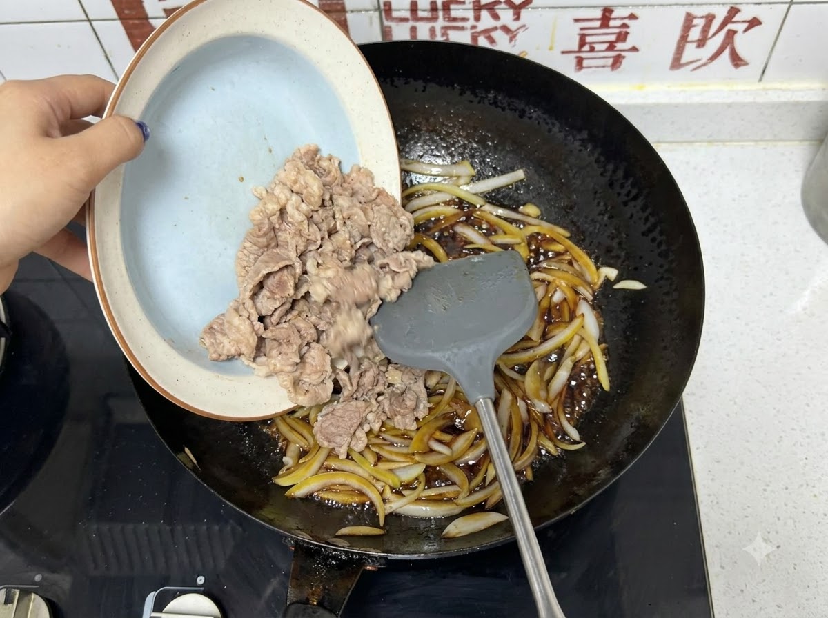 Pre-blanched beef slices being poured from a plate into a wok with onions and dark sauce.