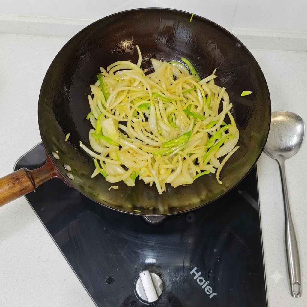 Slices of onions and green bell peppers being stir-fried in a hot black wok.