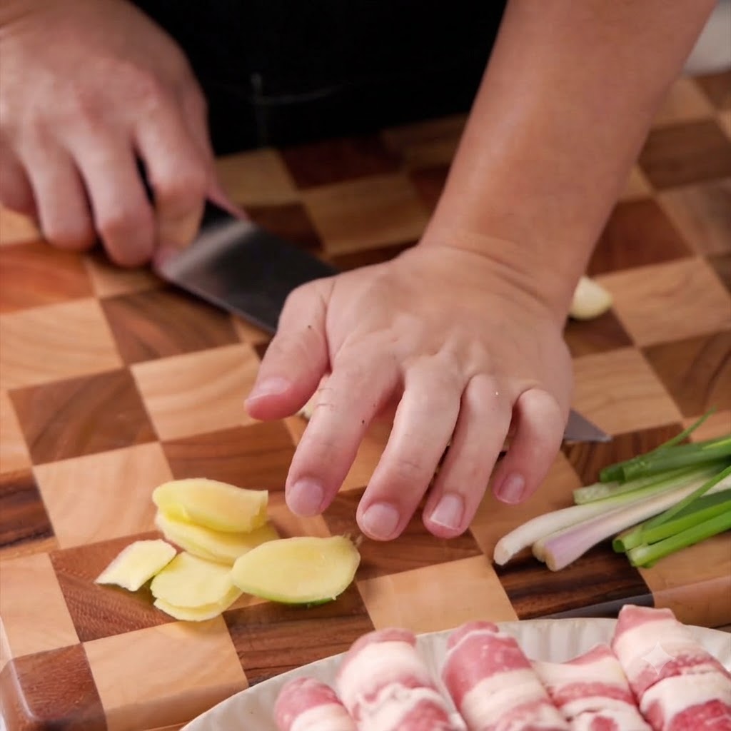 Garlic cloves being chopped and minced finely with a knife on a cutting board.