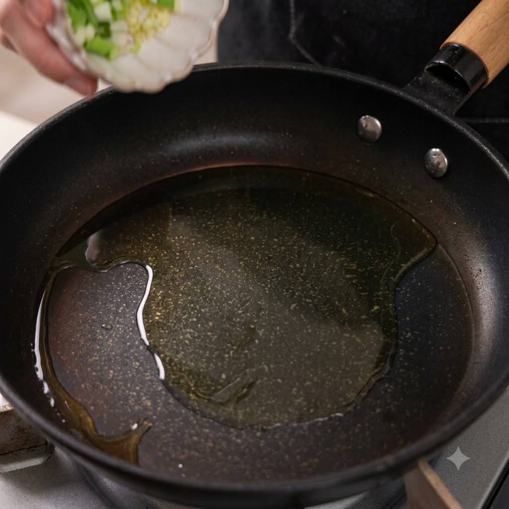 Minced garlic and chopped green onion whites dropping into a frying pan with heated oil.